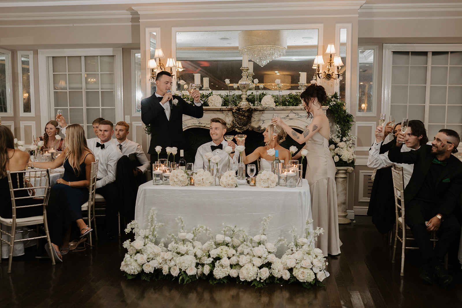 Best man and maid of honor raise their glasses to toast the newlyweds at their beautiful sweetheart table.